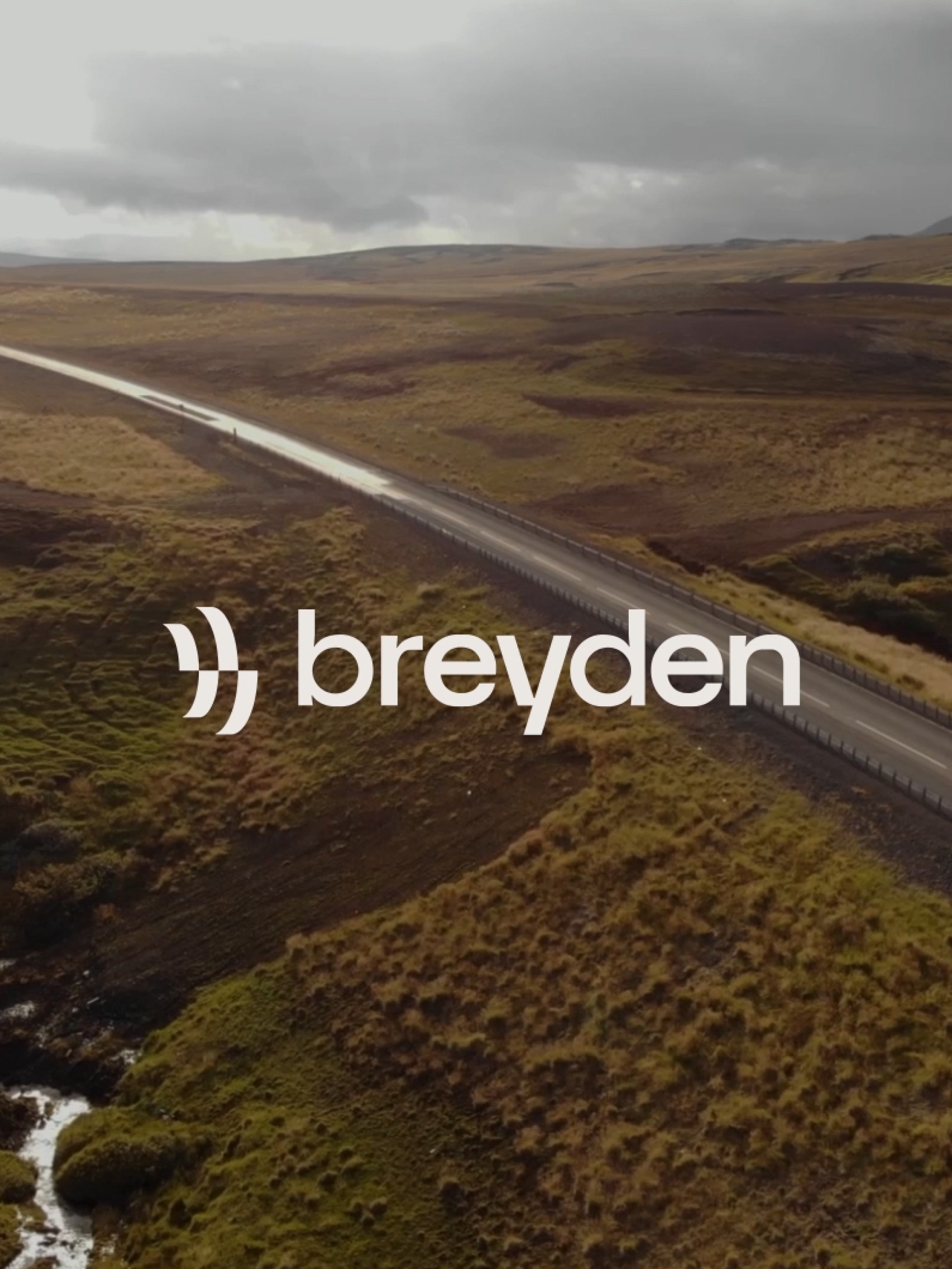 Luftaufnahme einer Straße mit dem Text „breyden“. Hügel und bewölkter Himmel.
