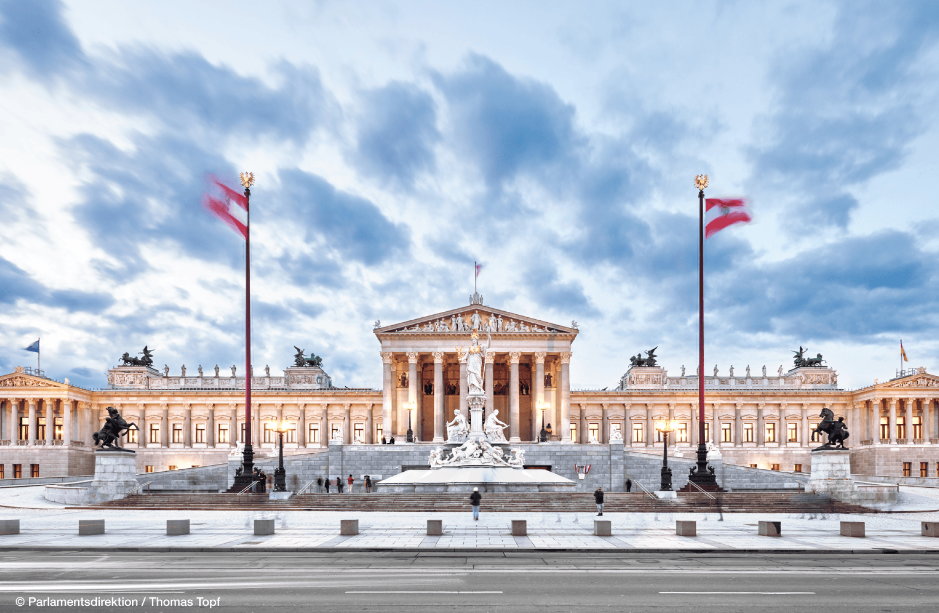 Außenansicht des österreichischen Parlamentsgebäudes in Wien mit zwei österreichischen Flaggen.