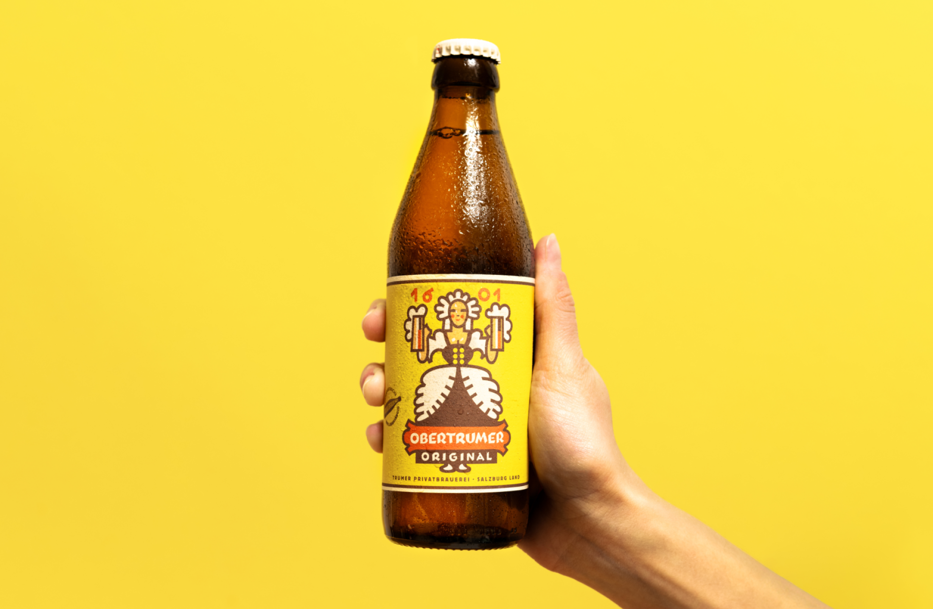 Eine Hand hält eine Flasche Obertrumer Original vor einem gelben Hintergrund.