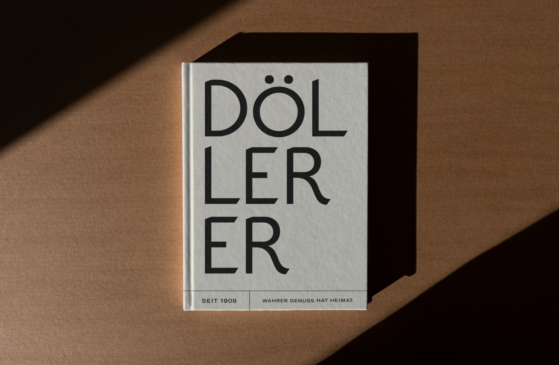 Das Buch "DÖLLERER" auf einem braunen Tisch, mit dem Text "SEIT 1909 WAHRER GENUSS HAT HEIMAT.".