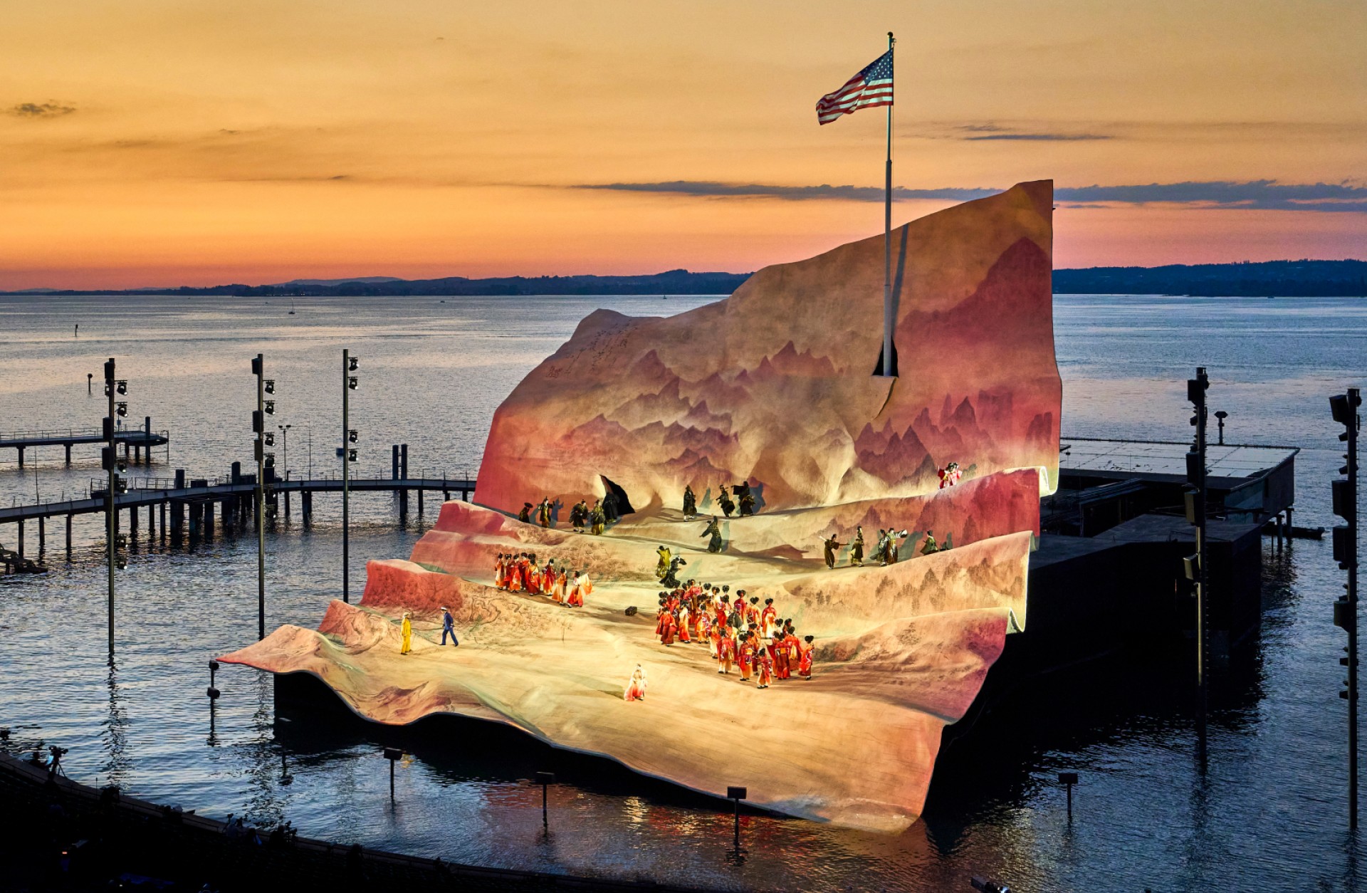 Eine Freilichtbühne auf dem Wasser, die mit einer US-Flagge und Darstellern in Kostümen für eine Aufführung ausgestattet ist.
