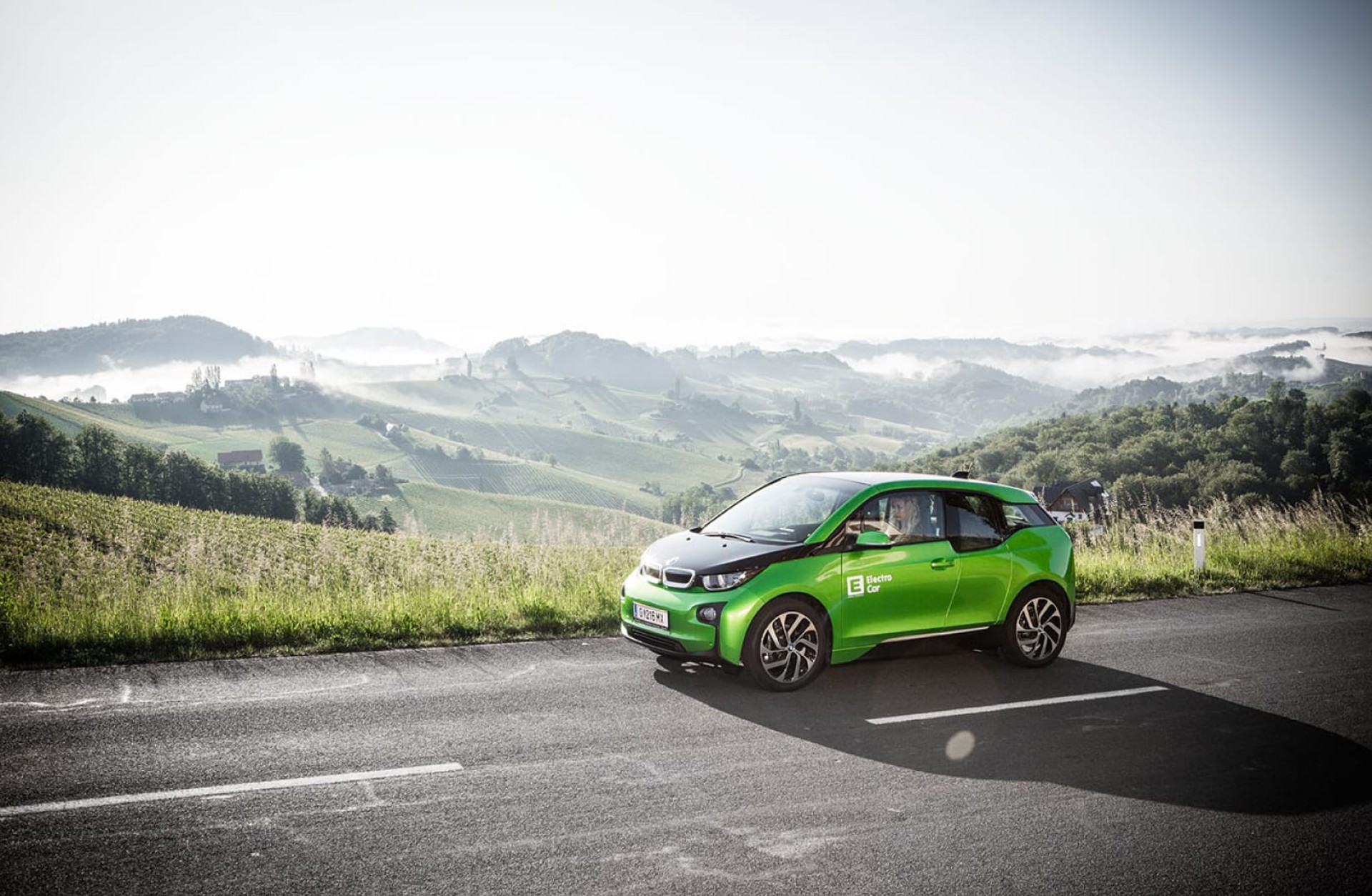 Grünes Elektroauto auf Asphaltstraße mit Blick auf Hügel. "Electro car" Text.