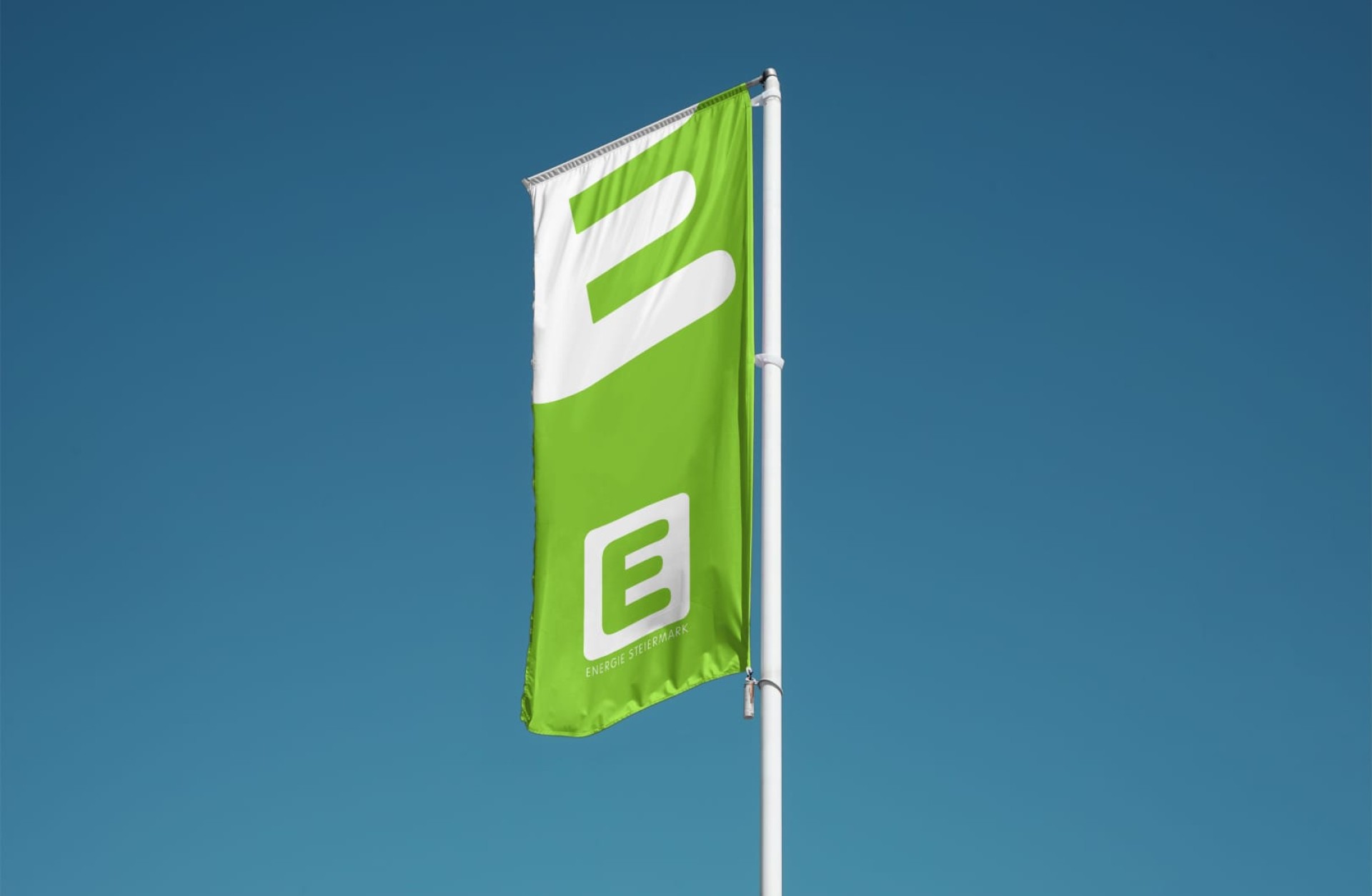 Grüne Flagge der Energie Steiermark mit weißem Logo vor blauem Himmel.