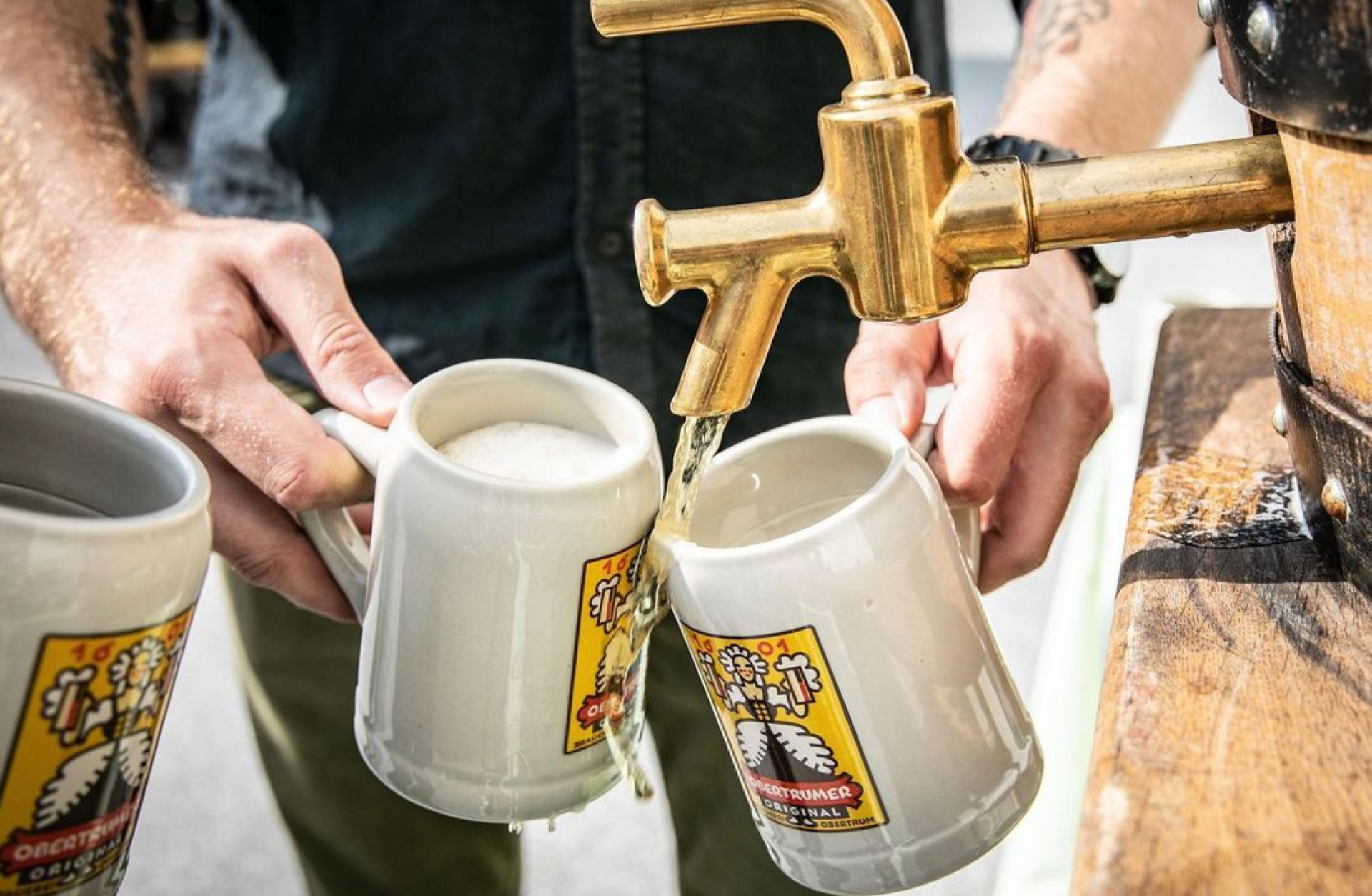 Zwei Hände füllen Bierkrüge mit OBERTRUMER ORIGINAL Bier aus einem goldenen Zapfhahn.