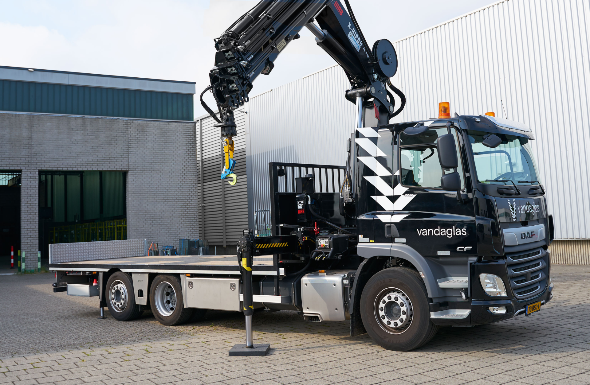 Ein schwarzer "vandaglas" DAF-Lkw mit Kran auf einem gepflasterten Bereich vor Gebäuden.