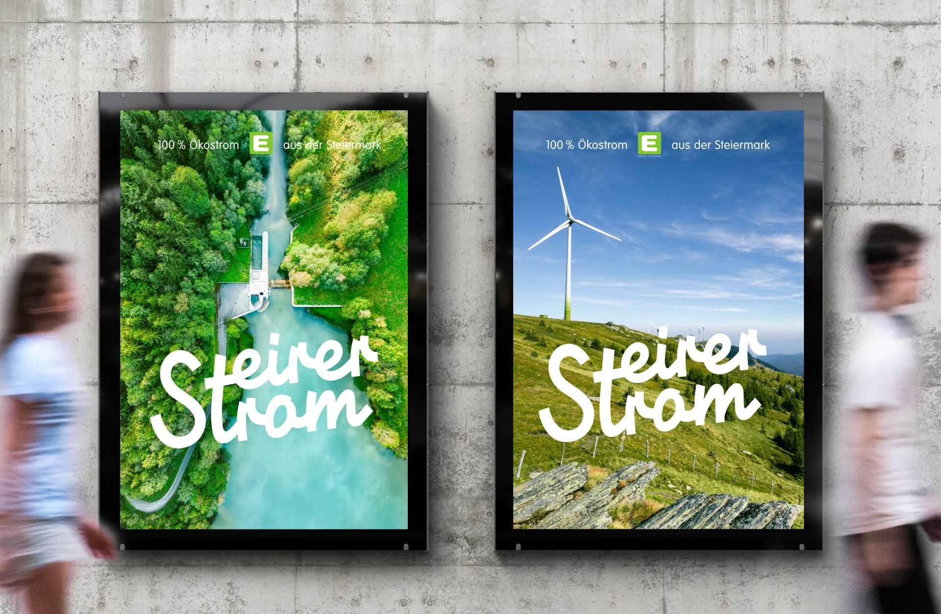 Zwei "Steirer Strom"-Poster mit Ökostrom-Motiven hängen an einer Betonwand. Menschen gehen vorbei.