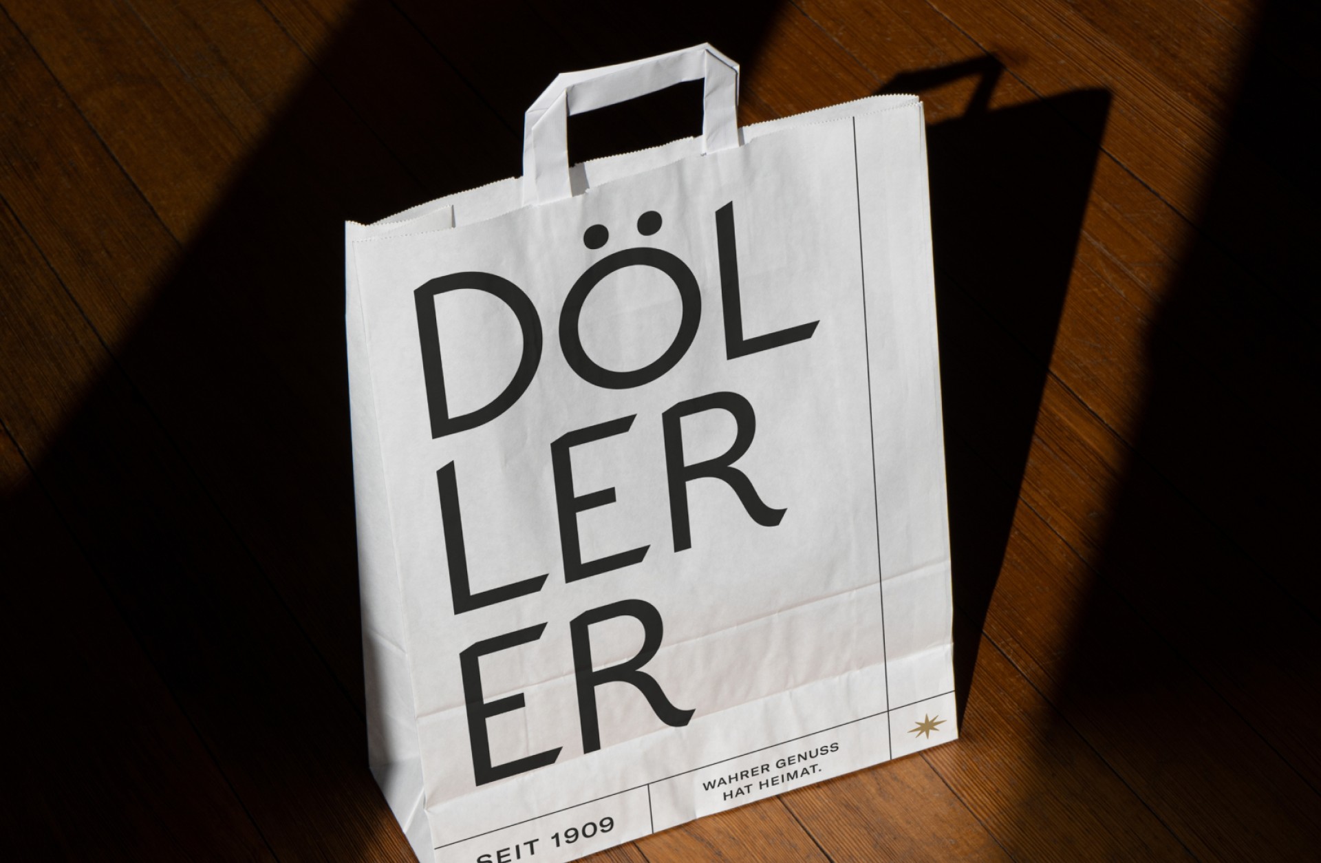 Eine weiße Döller-Papiertüte steht auf einem Holzboden. Aufdruck: "DÖLLER, SEIT 1909, WAHRER GENUSS HAT HEIMAT."