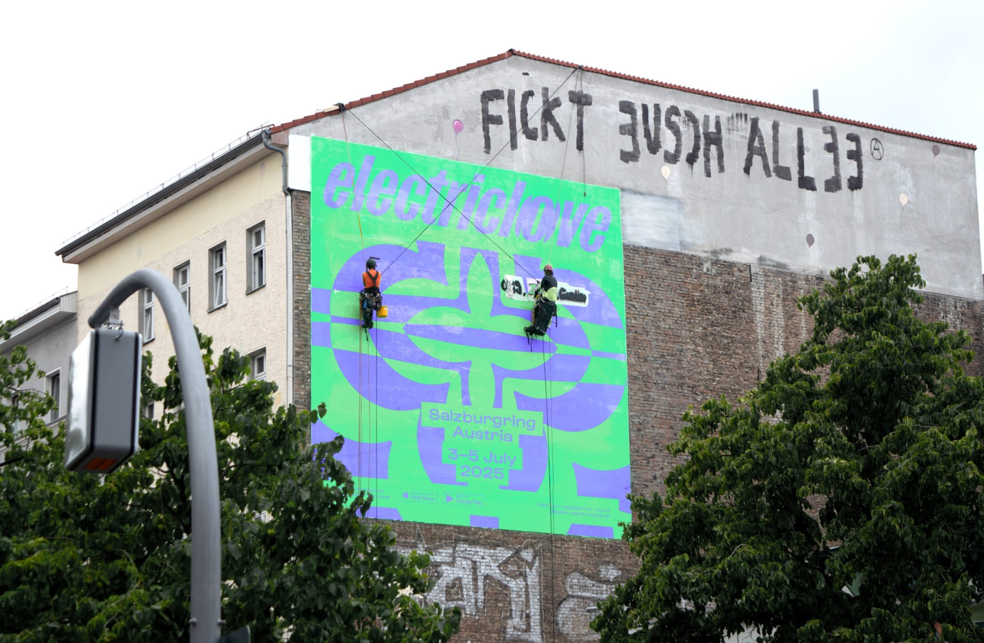 Zwei Arbeiter installieren ein "Electric Love Go"-Banner am Salzburggring, Österreich. Graffiti oben.