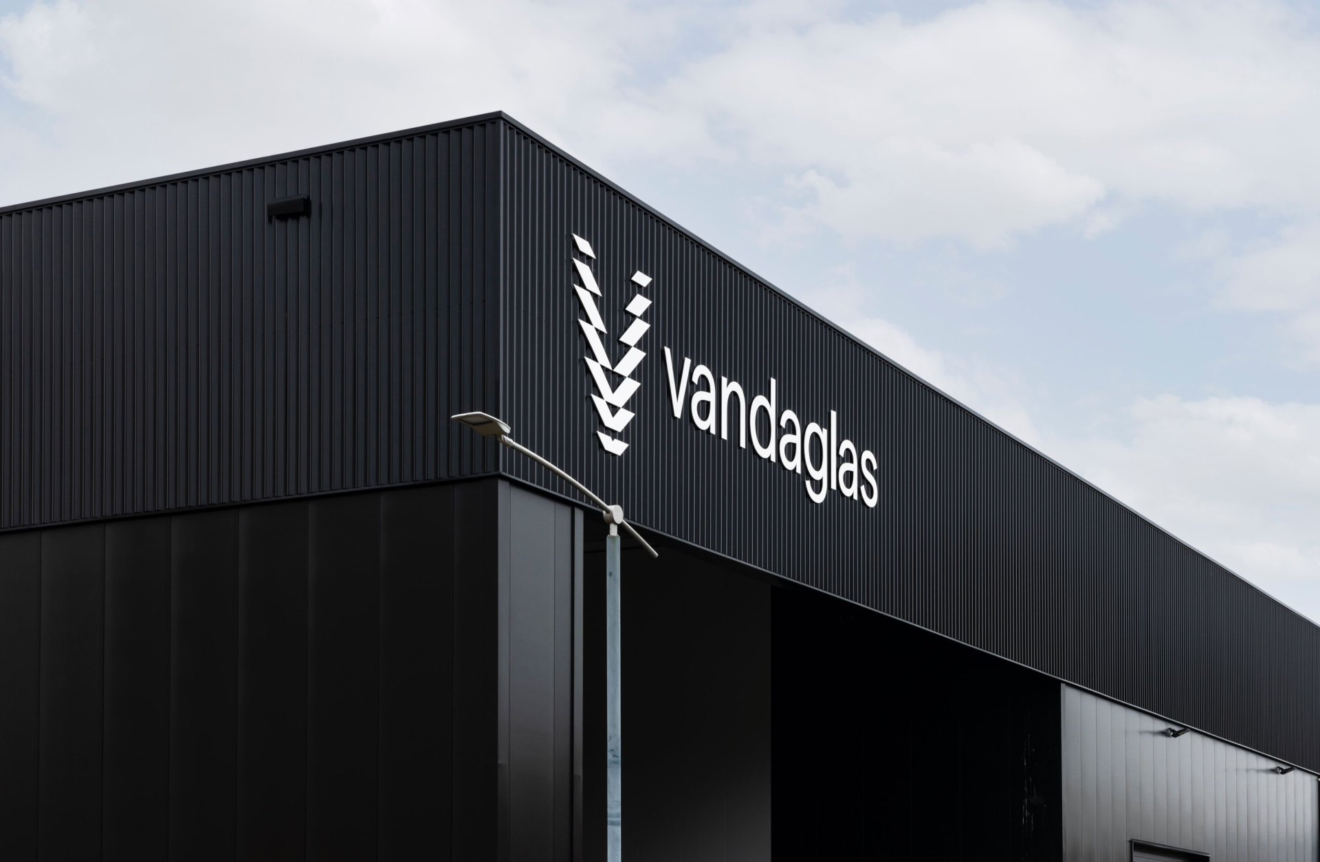 Schwarzes Gebäude mit weißem "vandaglas"-Logo und Symbol sowie einer Straßenlaterne davor.