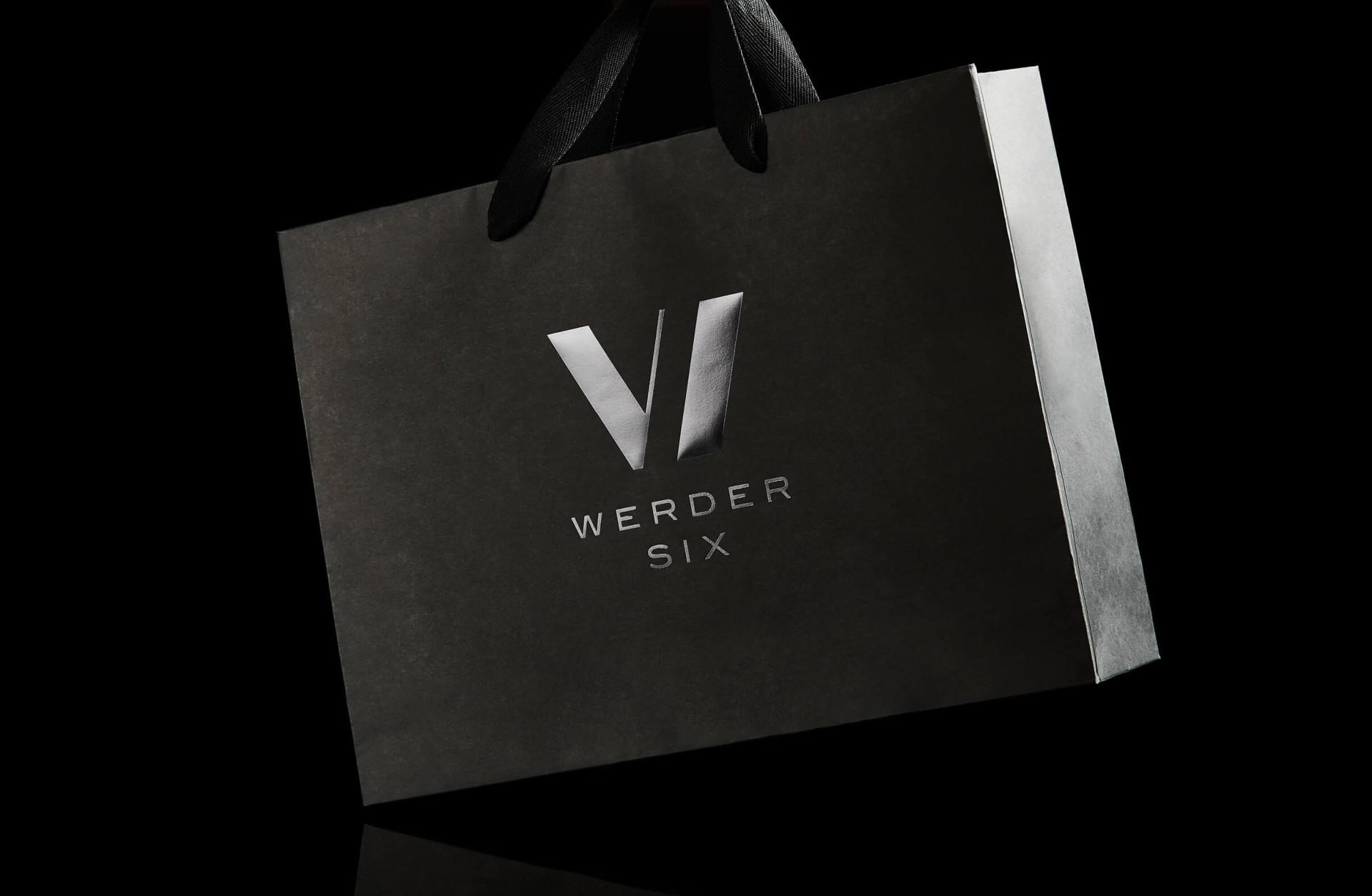 Eine schwarze Papiertüte mit dem silbernen Logo „VI WERDER SIX“ auf schwarzem Hintergrund.