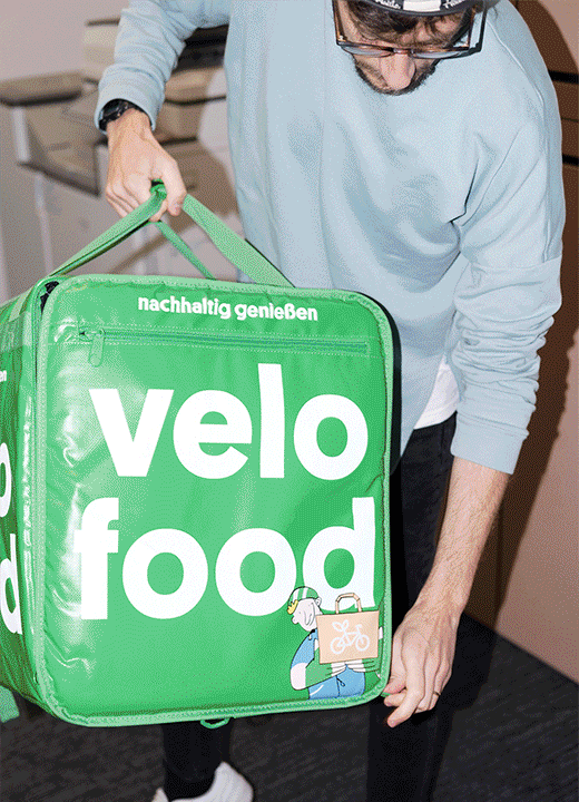 Eine Person hält eine grüne "velo food"-Liefertasche mit dem Slogan "nachhaltig genießen".
