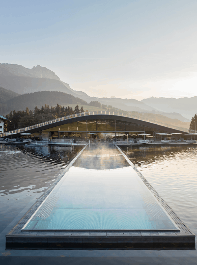 Blick auf das Hotel Seehof in Österreich mit einem Seebecken und Bergen im Hintergrund.